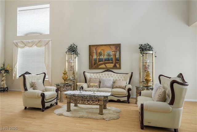 living area featuring light wood-style flooring, a high ceiling, and baseboards