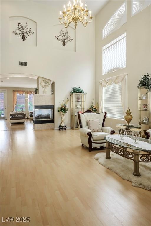 sitting room featuring a chandelier, wood finished floors, a towering ceiling, visible vents, and a tiled fireplace