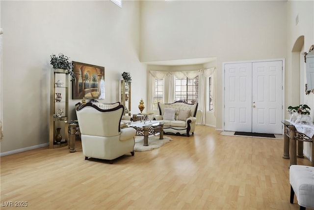 sitting room with arched walkways, a high ceiling, wood finished floors, and baseboards