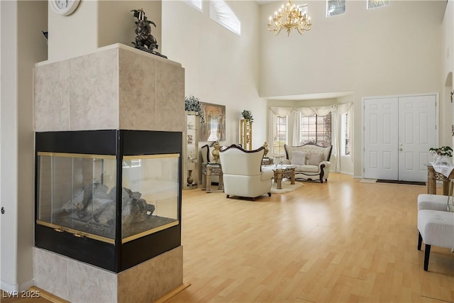 living room with a notable chandelier, a towering ceiling, a multi sided fireplace, and wood finished floors