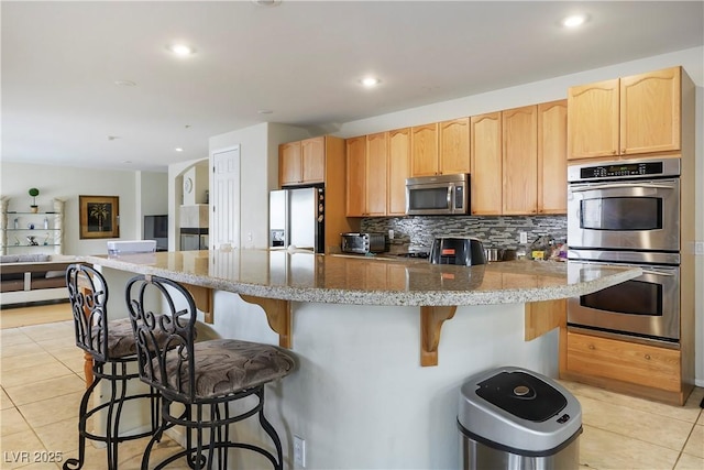 kitchen featuring light stone counters, light tile patterned floors, stainless steel appliances, decorative backsplash, and light brown cabinetry