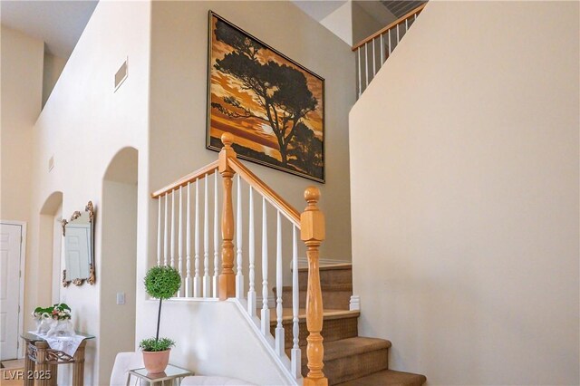 stairway featuring arched walkways, a high ceiling, and visible vents