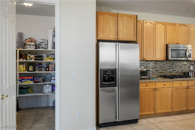 kitchen featuring light stone counters, light tile patterned flooring, a toaster, stainless steel appliances, and backsplash