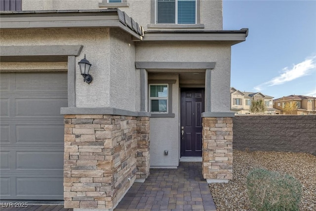 view of exterior entry featuring a garage, stone siding, and stucco siding