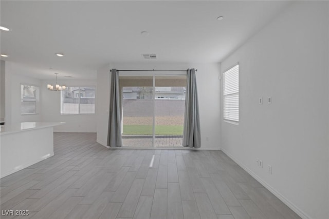 unfurnished living room with baseboards, visible vents, an inviting chandelier, and wood finished floors