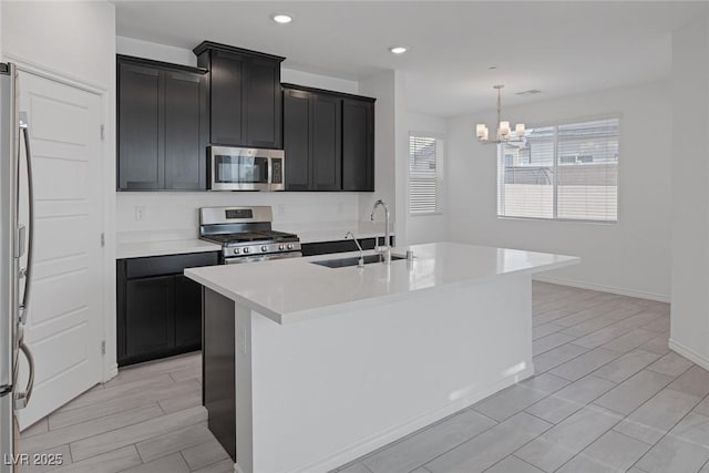 kitchen with stainless steel appliances, a sink, light countertops, a center island with sink, and an inviting chandelier