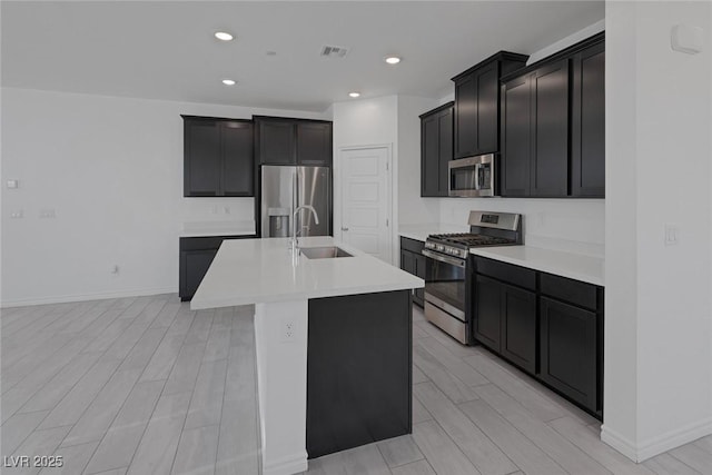 kitchen featuring wood finish floors, a center island with sink, stainless steel appliances, light countertops, and a sink