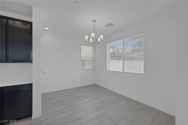 unfurnished dining area featuring baseboards, light wood-type flooring, visible vents, and an inviting chandelier