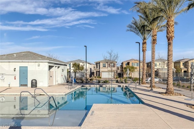 community pool with a patio area, fence, and a residential view