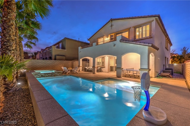 pool at dusk with a patio, a fenced backyard, and a pool with connected hot tub