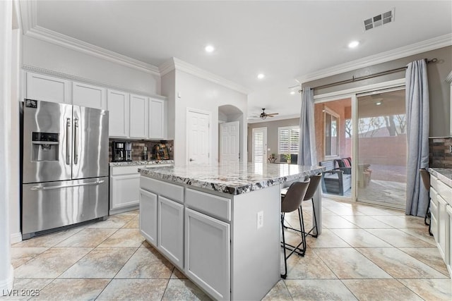 kitchen featuring a kitchen island, visible vents, stainless steel refrigerator with ice dispenser, backsplash, and light stone countertops