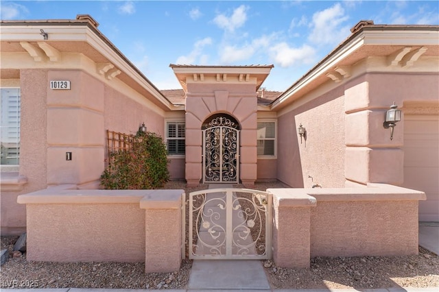 doorway to property featuring an attached garage, a gate, fence, and stucco siding