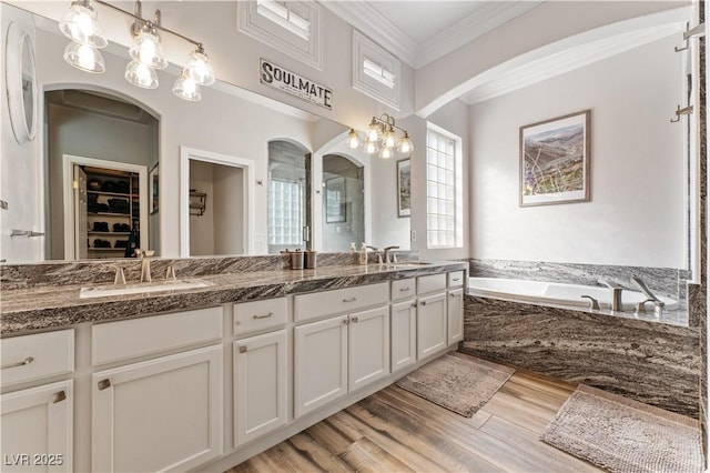 full bath with a sink, double vanity, crown molding, and wood finished floors