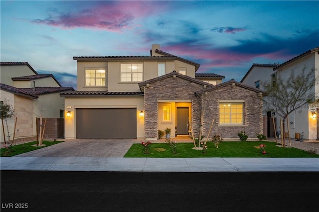 mediterranean / spanish-style house with an attached garage, stone siding, decorative driveway, stucco siding, and a front lawn