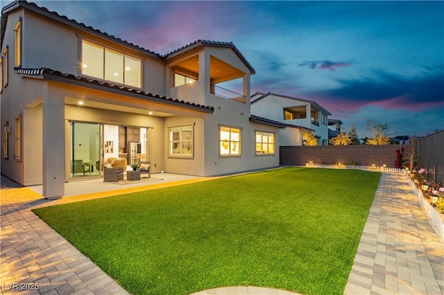 back of property at dusk featuring a yard, a patio, a fenced backyard, and stucco siding