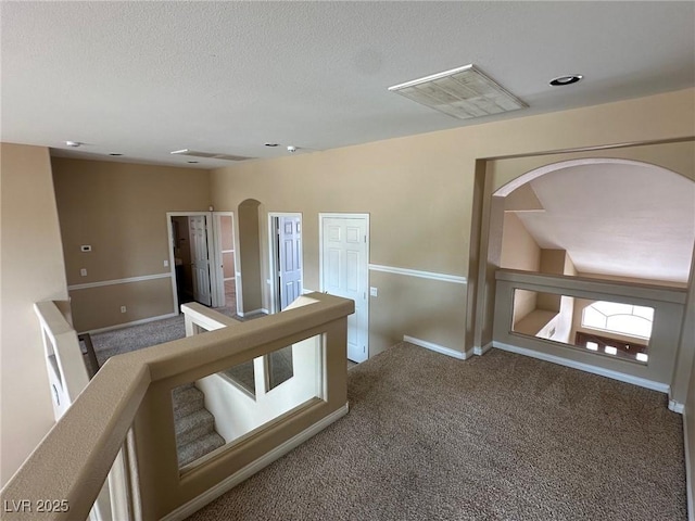 hall with baseboards, visible vents, arched walkways, a textured ceiling, and carpet floors