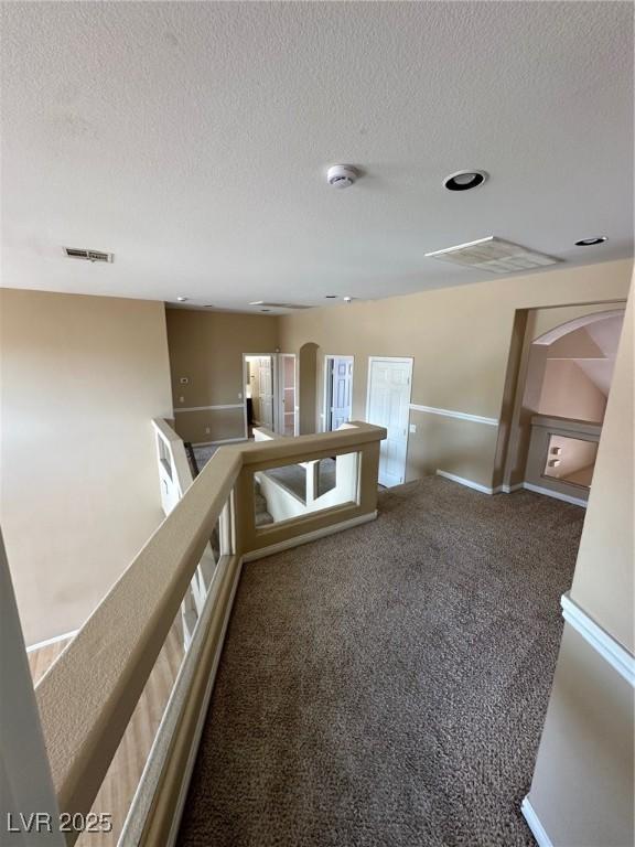 hall featuring arched walkways, a textured ceiling, carpet floors, an upstairs landing, and visible vents