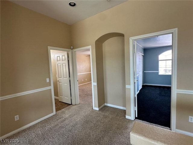 hall with arched walkways, carpet, and baseboards