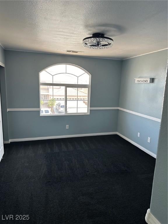 unfurnished room featuring a textured ceiling, dark colored carpet, visible vents, and baseboards