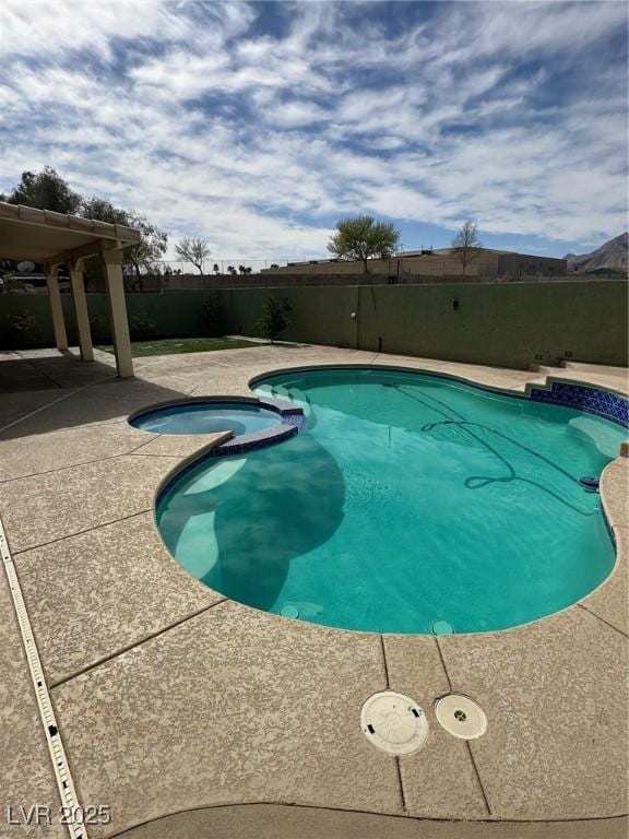 view of swimming pool with a patio area, a pool with connected hot tub, and fence