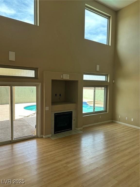 unfurnished living room with a towering ceiling, light wood finished floors, a fireplace with flush hearth, and a wealth of natural light