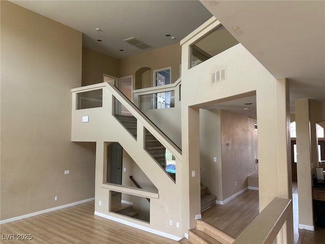 stairway featuring a towering ceiling, wood finished floors, visible vents, and baseboards