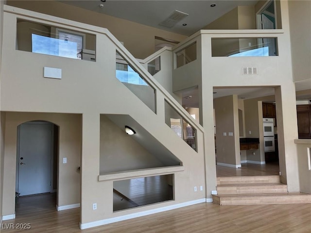 stairs featuring arched walkways, visible vents, a towering ceiling, wood finished floors, and baseboards