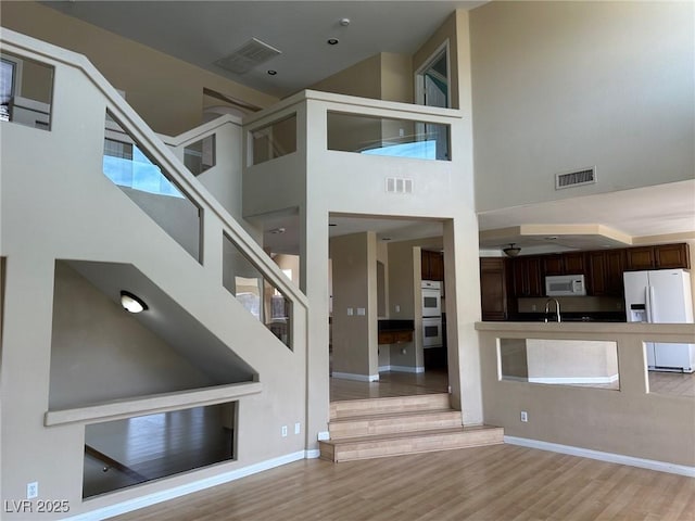 interior space with light wood finished floors, a towering ceiling, and visible vents