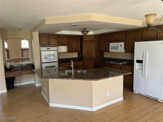 kitchen featuring white appliances, wood tiled floor, dark stone counters, and a sink