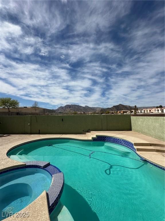 view of swimming pool with a pool with connected hot tub, fence, and a mountain view