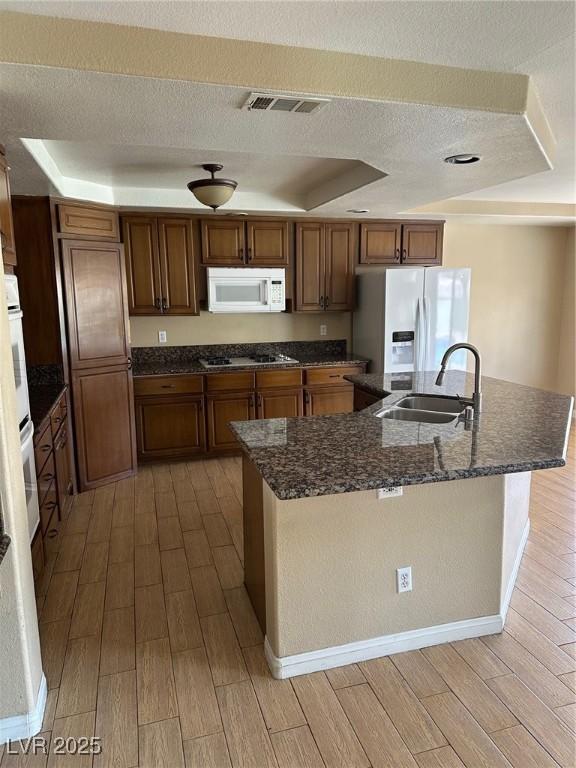 kitchen featuring white appliances, visible vents, a raised ceiling, wood tiled floor, and a sink