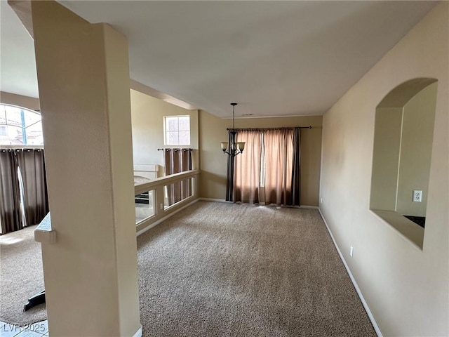 empty room featuring carpet floors, baseboards, and a chandelier