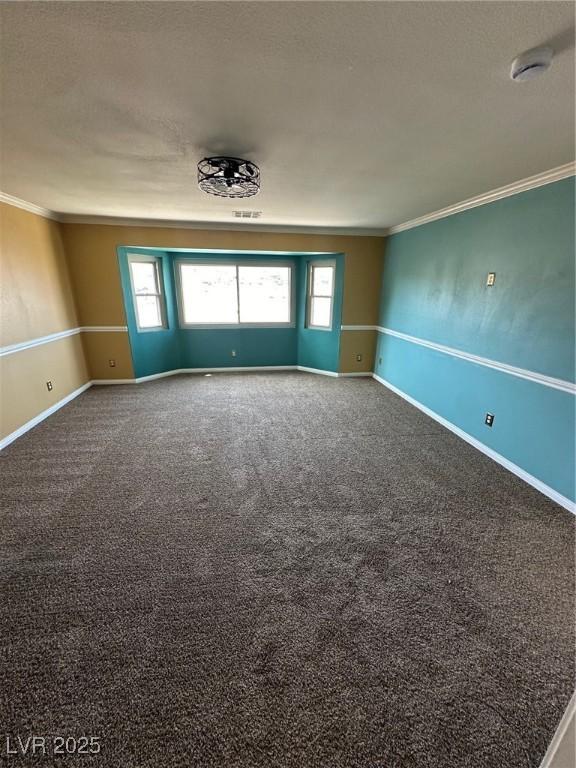 unfurnished room featuring a textured ceiling, ornamental molding, carpet, and baseboards