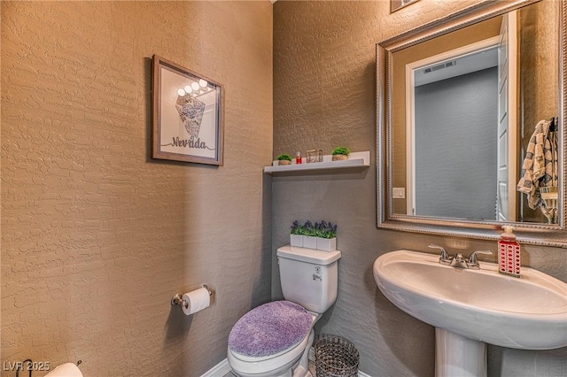 half bath featuring a textured wall, a sink, and toilet