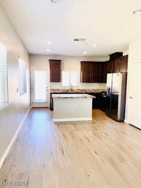 kitchen with white refrigerator with ice dispenser, visible vents, a kitchen island, dark brown cabinets, and light wood-style floors