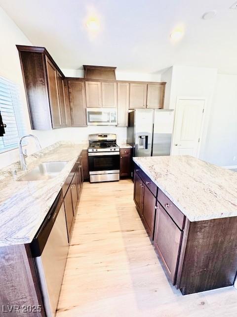 kitchen with light wood finished floors, appliances with stainless steel finishes, light stone counters, a center island, and a sink