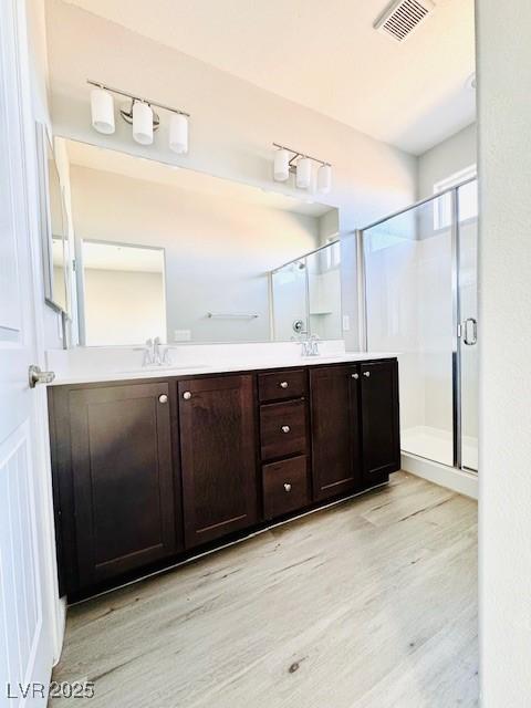 bathroom featuring a sink, a stall shower, wood finished floors, and visible vents