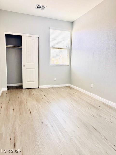 unfurnished bedroom with light wood finished floors, baseboards, visible vents, and a closet