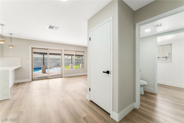 hallway featuring baseboards, visible vents, and light wood finished floors