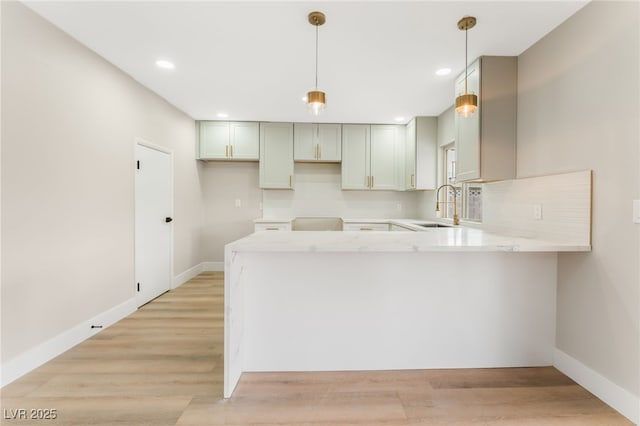 kitchen with light wood-style flooring, backsplash, a sink, a peninsula, and baseboards