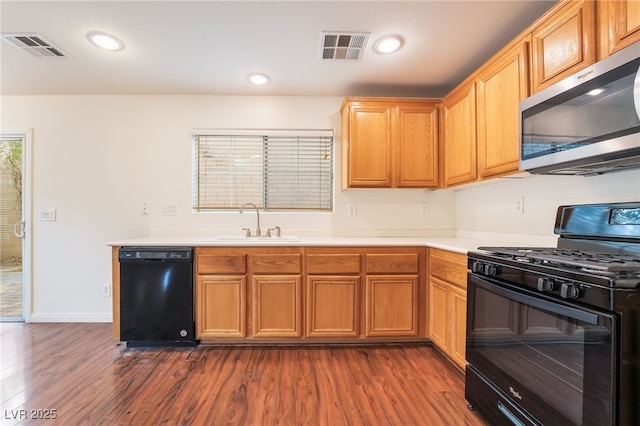 kitchen with dark wood-style flooring, visible vents, a sink, and black appliances