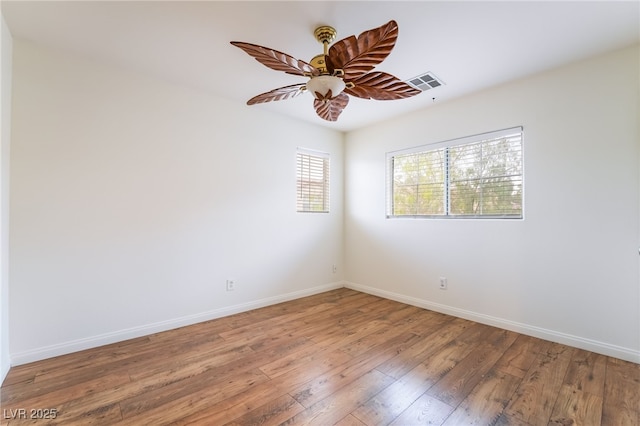 empty room with a ceiling fan, hardwood / wood-style flooring, visible vents, and baseboards