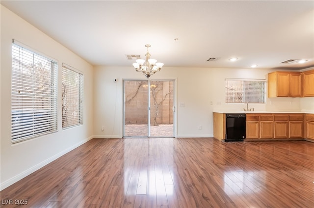 unfurnished dining area with visible vents, an inviting chandelier, a sink, wood finished floors, and baseboards