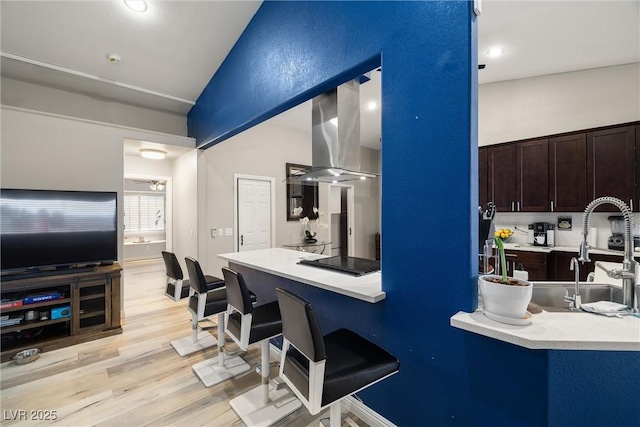 kitchen featuring dark brown cabinets, light wood-style floors, island range hood, black electric cooktop, and a sink