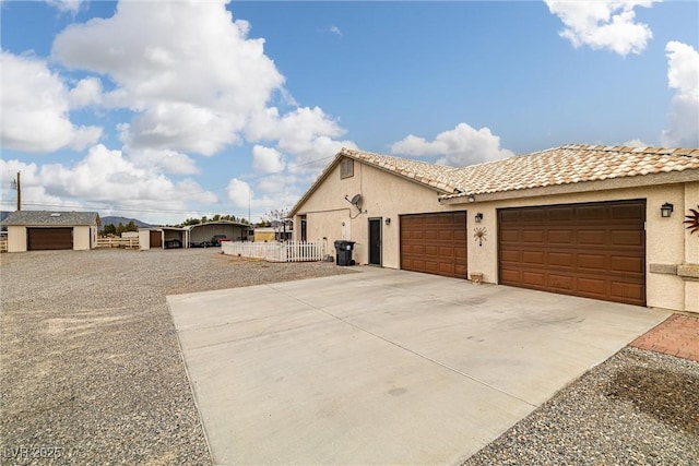 view of home's exterior with fence, a tile roof, concrete driveway, stucco siding, and a garage