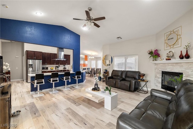 living area with light wood-type flooring, visible vents, a tile fireplace, and vaulted ceiling