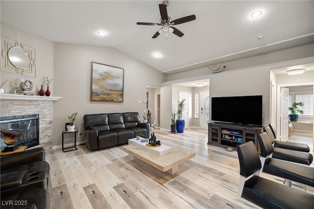 living room with baseboards, a fireplace, ceiling fan, vaulted ceiling, and light wood-style floors