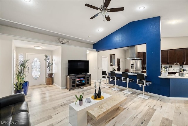 living room with baseboards, lofted ceiling, light wood-style flooring, and a ceiling fan