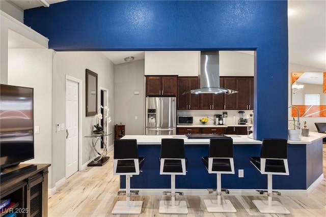 kitchen featuring stainless steel refrigerator with ice dispenser, a breakfast bar area, light countertops, extractor fan, and dark brown cabinets