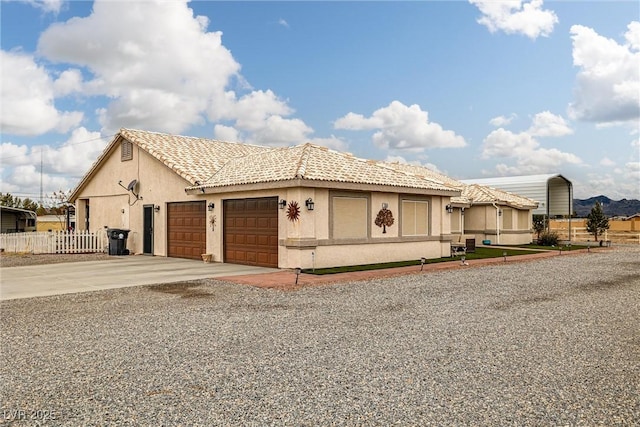 view of front facade with an attached garage, fence, a tiled roof, stucco siding, and driveway